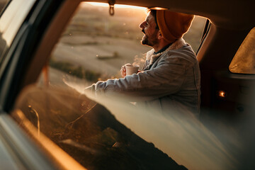Fototapeta na wymiar A man sits in the trunk of a car and drinks a fresh hot coffee by himself. Enjoying the nature view