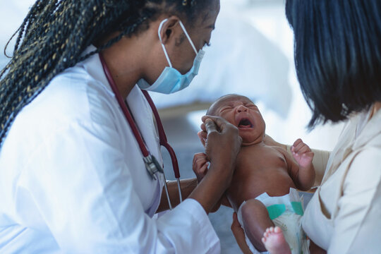 African Doctor checking sick newborn baby, baby unhappy and crying, Mom looks on with concern