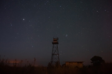 Night scene, old border observation tower against the background of a starry sky, photo with low lighting and soft focus.
