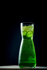 Green lemonade with lime and ice in a decanter on a dark background