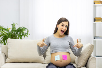Photo of positive pregnant woman with pink and blue papers on the stomach which mean gender of...