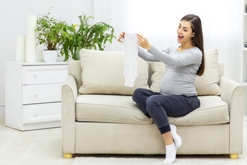 Photo of pregnant woman holding child small clothes.