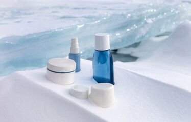 Cosmetic products for face and hand skin care in cold winter time. Advertising of nourishing reparative natural cosmetics on podium stand from snowy crust against background of ice of frozen lake