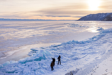Baikal Lake in winter at sunset. Group of tourists inspects high ice heaps and blue icy hummocks...
