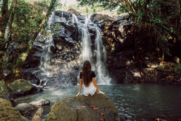 Traveller woman sitting on stone and waterfall in Bali island