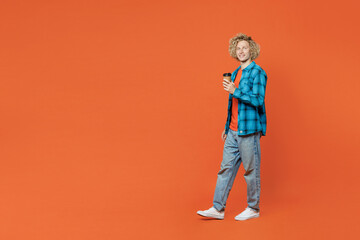 Full body side view young blond man wear blue shirt orange t-shirt hold takeaway delivery craft paper brown cup coffee to go isolated on plain red background studio portrait. People lifestyle concept.