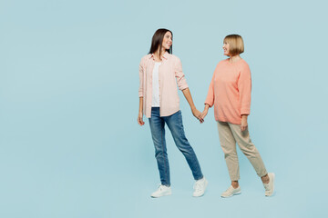 Full body side view fun elder parent mom with young adult daughter two women together wearing casual clothes hold hands walk go look to each other isolated on plain blue background Family day concept