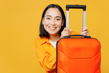 Young smiling woman wears summer casual clothes near suitcase look camera isolated on plain yellow...