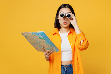 Young amazed woman in summer casual clothes hold in hand map use binoculars isolated on plain...