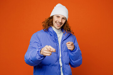 Young confident man with long curly hair wear hat purple ski padded jacket casual clothes point index finger camera on you motivating encourage isolated on plain orange red background studio portrait.