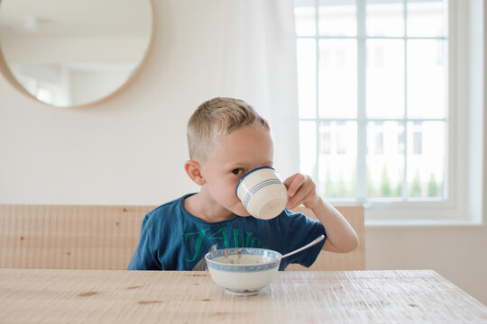 portrait of a young boy looking with one eye drinking at breakfast