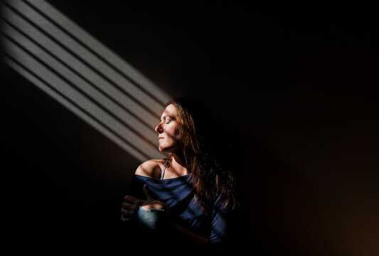 Profile of woman with eyes closed in a patch of light a dark room.
