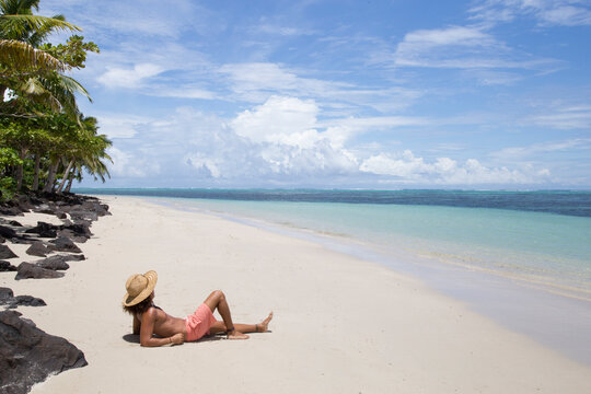 One tanned man, with hat,  laying on white sand tropical beach