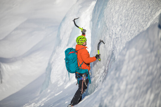 Ice climber swings his ice axe into a glacial serac while climbing.