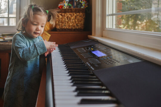 a cute little girl in pigtails plays on a keyboard in front of window