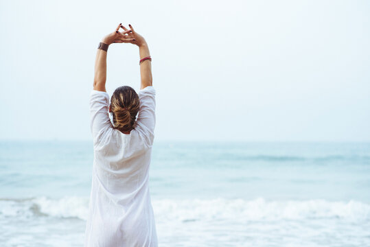 Woman with her back and white dress doing stretching on the beach.