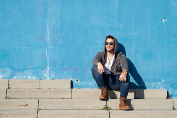 Portrait of stylish man sitting on stairs leaning on a blue wall