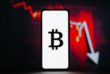 Bitcoin icon on smartphone against background of red down arrow and stock chart. Stock price fall, scam, cryptocurrency crisis and investment crash concept