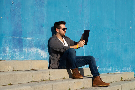 Side view of a young man with sunglasses sitting on stairs while using a tablet pc