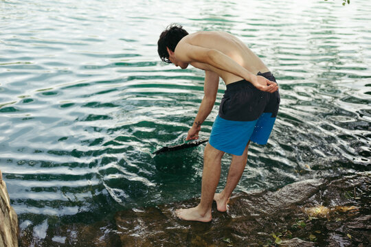 Young man in beach shorts washing grill in a river