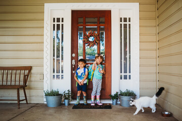 Young boy and girl standing outside front door wearing back packs