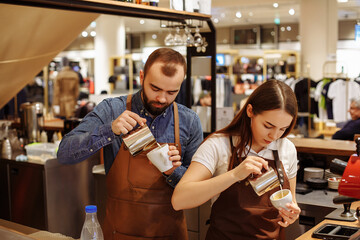 Two bartenders, a girl and a boy, prepare coffee drinks