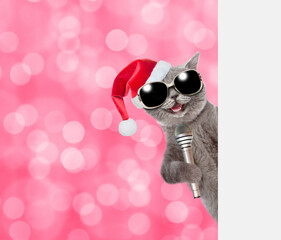 Happy cat wearing red christmas hat holds microphone behind empty white banner with festive background. Shade trendy color of the year 2023 - Viva Magenta background. Empty space for text