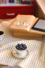 Plate of cookies, cup of tea, fresh blueberries, dry oranges, stack of books, reading glasses and tablet on the table. Hygge at home. Selective focus.