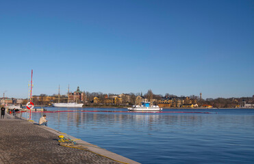 Fototapeta premium Pier at the bay Strömmen with commuting harbor ferry and the steel hostel sail ship af Chapman, a sunny winter day in Stockholm