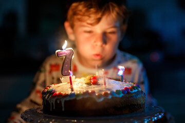 Adorable happy blond little kid boy celebrating his birthday. Child blowing seven candles on...