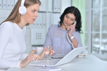 Young businesswoman in headphones working in modern office with her olleague
