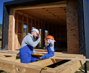 Father with toddler son building wooden frame house. Male builder giving high five to kid on...