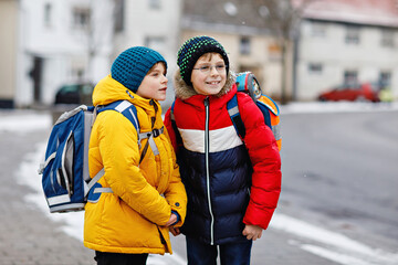 Two little kids boys of elementary class walking to school during snowfall. Happy children having...