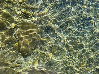 Sea water clear surface with pebbles, sand, stones at the bottom.