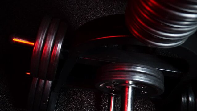 Close-up of chrome steel bar with black weight plate on the training apparatus in the gym. Body training and fitness for healthy lifestyle. High quality FullHD footage. Red neon light