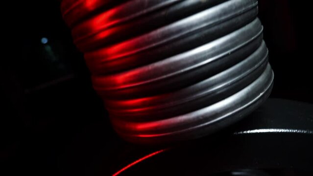 Close-up of chrome steel bar with black weight plate on the training apparatus in the gym. Body training and fitness for healthy lifestyle. High quality FullHD footage. Red neon light