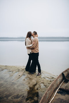 man and woman hugging on the lake shore, cold foggy weather. romantic photo in beige clothes. to hug a woman, a love story. beige sweaters. romantic photos against the background of a foggy lake