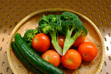Close up high angle view of a group of fresh vegetables produce drying in bamboo sieve after being washed; visible water droplets. Beam of sunlight hits the basket, natural lighting
