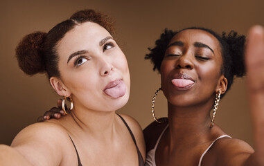 Beauty, friends and tongue with selfie of black women for social media, skincare and fashion. Happy, silly and picture with funny face of girl for internet, comic and crazy in brown background studio