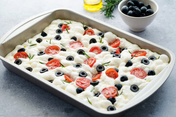 Traditional Italian Focaccia Bread no baked with rosemary, tomatoes, olives, sea salt and olive oil in baking dish. Healthy food concept. top view