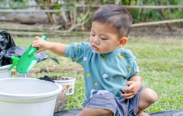 Little child shovels soil into pots to prepare plants for planting. Toddler boy digging soil for...