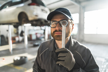 Repair shop worker looking through a hole in a spanner. Medium shot. Blurred background. High...