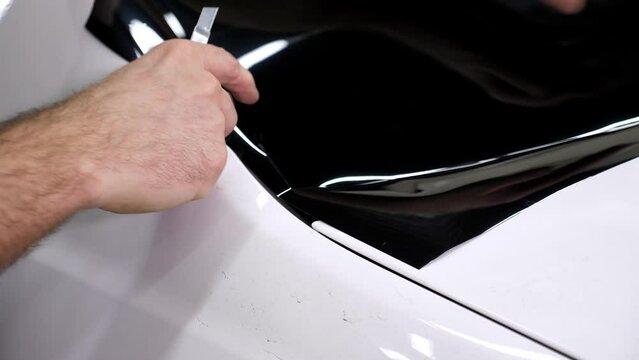 The car mechanic cuts off the excess tinting foil when gluing on the car glass in the garage. Installing car window tint.
