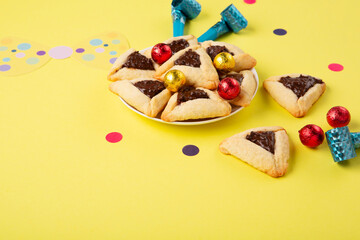 Hamantaschen Cookies, Carnival Mask, Noisemaker on Yellow Background. Purim Celebration, Jewish Carnival Holiday Concept.
