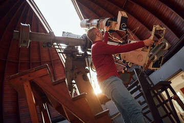 Astronomer with a big astronomical telescope in observatory doing science research.