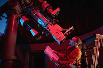 Astronomer with a big astronomical telescope in observatory doing science research of space and...