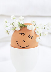 Easter egg with cute face in floral wreath crowns in egg cup on white background.