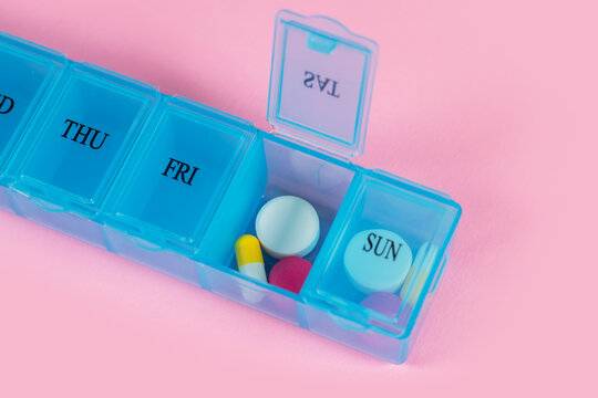 Pill organizer with variety of pills and supplement. Weekly Pill Organizer on pink background.