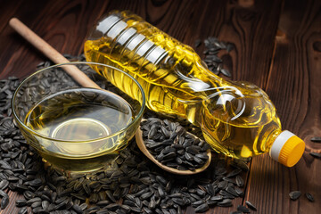 Sunflower oil in glass bowl and bottle with seed in wooden spoon on wooden background