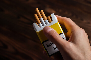 A mans hand holding out an open pack of cigarettes